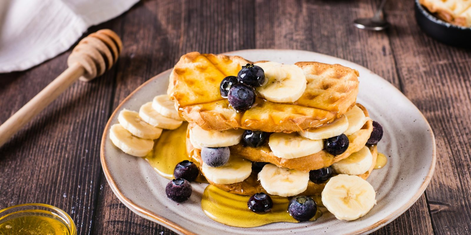 A stack of waffles with banana, blueberries and honey on a plate. Comfort food.