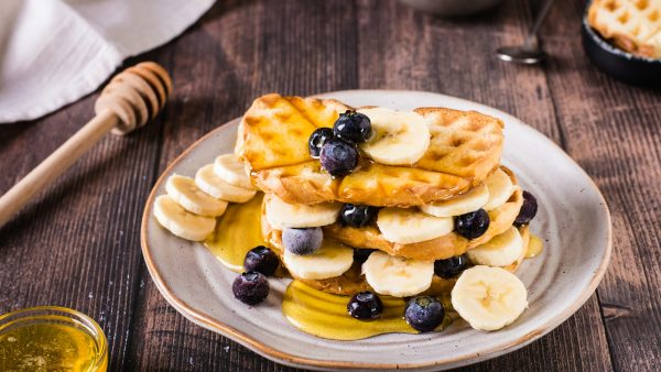 A stack of waffles with banana, blueberries and honey on a plate. Comfort food.