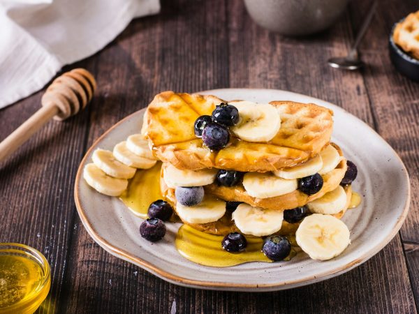 A stack of waffles with banana, blueberries and honey on a plate. Comfort food.