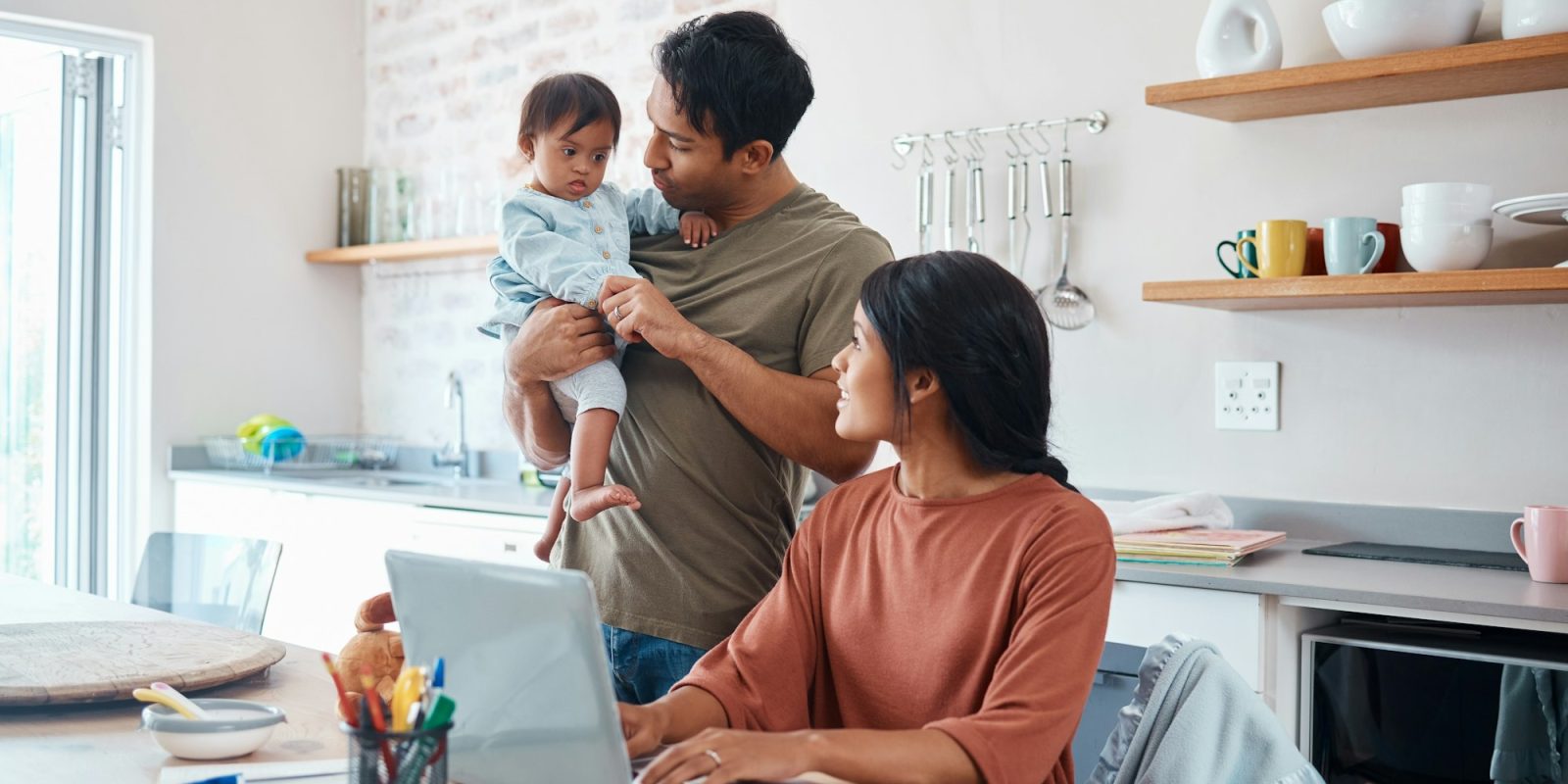 Family, baby and down syndrome while mother work online with laptop in kitchen. Mom, father and chi