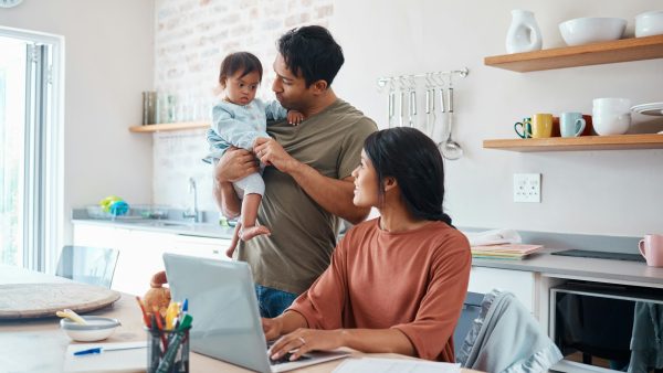 Family, baby and down syndrome while mother work online with laptop in kitchen. Mom, father and chi