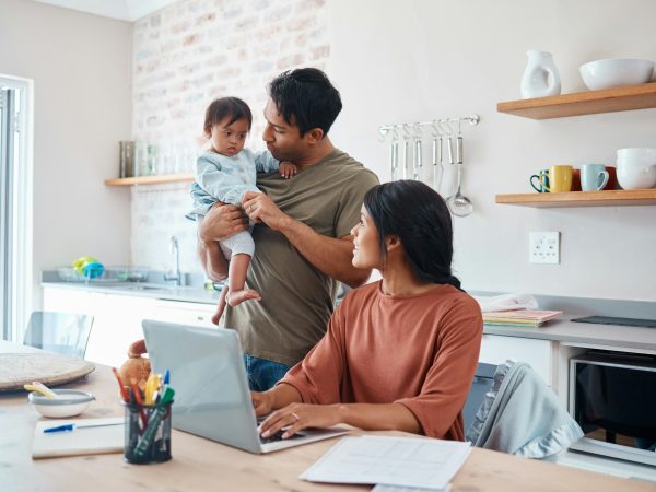 Family, baby and down syndrome while mother work online with laptop in kitchen. Mom, father and chi