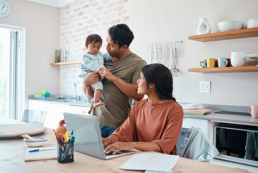 Family, baby and down syndrome while mother work online with laptop in kitchen. Mom, father and chi