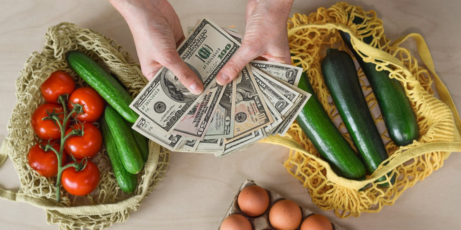 Female hands holding US American cash money with reusable grocery bags with fresh produce on counter