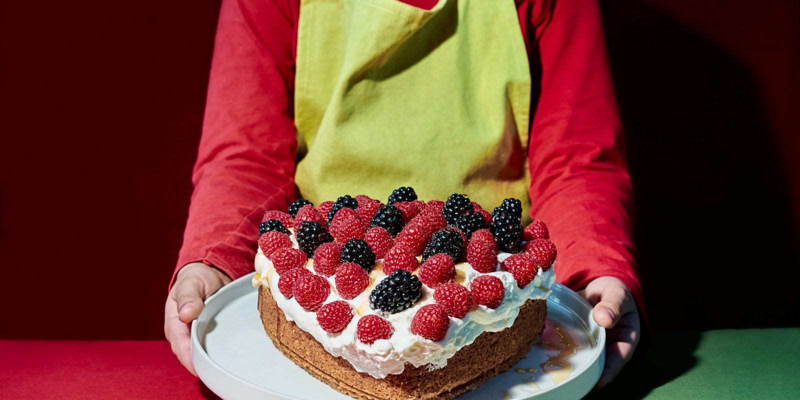 Valentine's Day. Child with apron pouring syrup on a heart-shaped cake