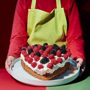 Valentine's Day. Child with apron pouring syrup on a heart-shaped cake