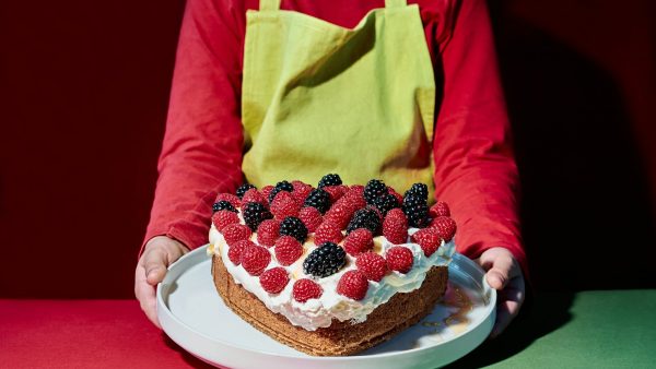 Valentine's Day. Child with apron pouring syrup on a heart-shaped cake