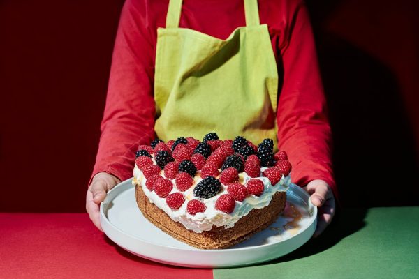 Valentine's Day. Child with apron pouring syrup on a heart-shaped cake