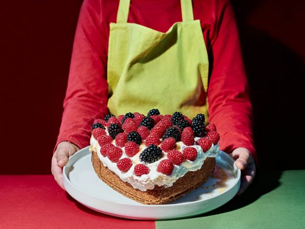 Valentine's Day. Child with apron pouring syrup on a heart-shaped cake