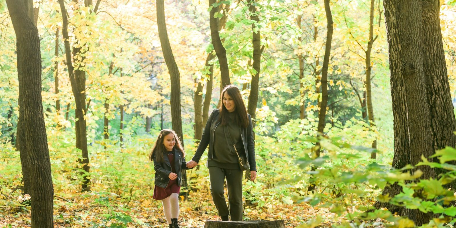 Young woman and her child girl walking through park. Single parent and motherhood concept