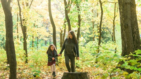 Young woman and her child girl walking through park. Single parent and motherhood concept