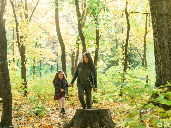 Young woman and her child girl walking through park. Single parent and motherhood concept