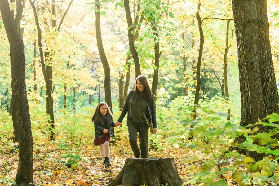 Young woman and her child girl walking through park. Single parent and motherhood concept