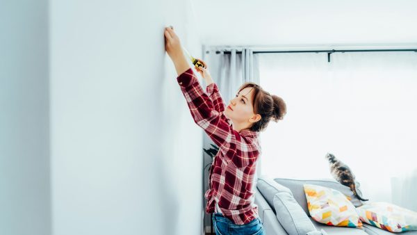 Young woman in plaid shirt doing measuring with measure tape on the wall. Doing repair herself. DIY